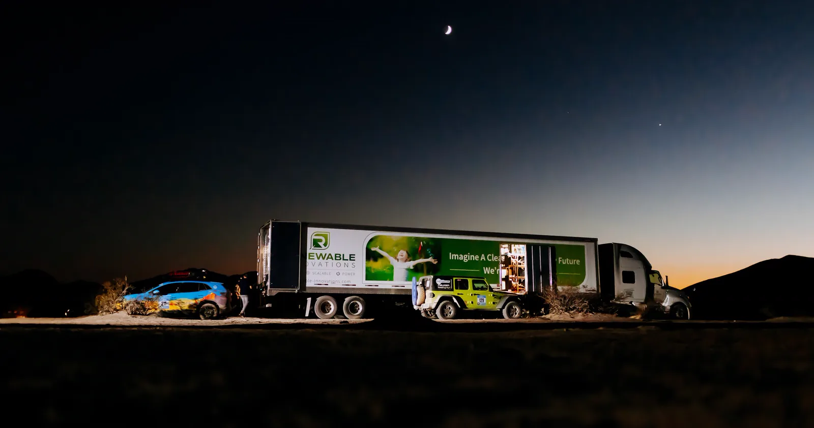 The Renewable Innovations semi trailer at night in the desert, charging rally vehicles under a crescent moon